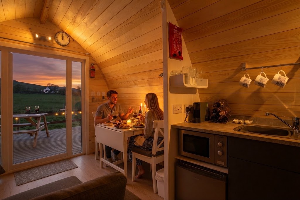 Earth-sheltered glamping burrow with a grass roof and round door built into a Cumbrian hillside above a lake