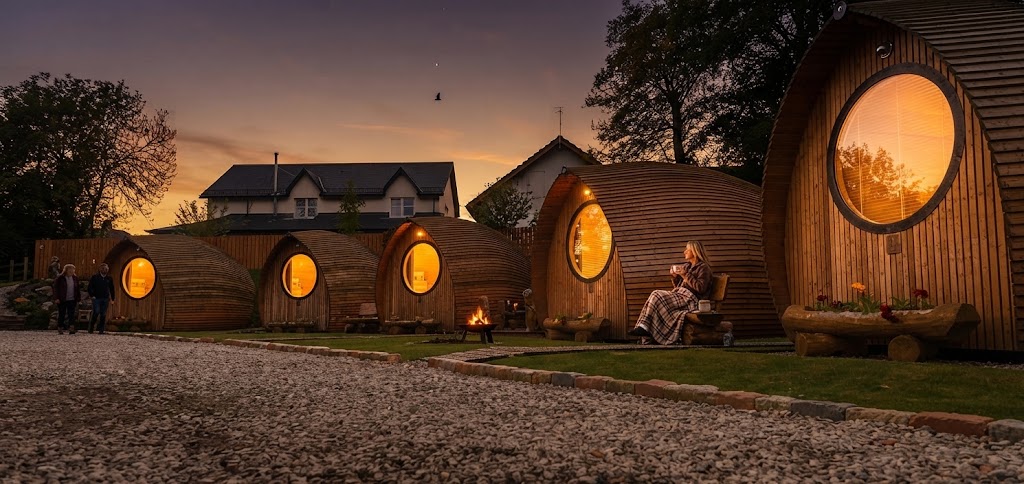 Wood-fired barrel hot tub with steam rising, positioned on decking beside a timber glamping cabin at dusk
