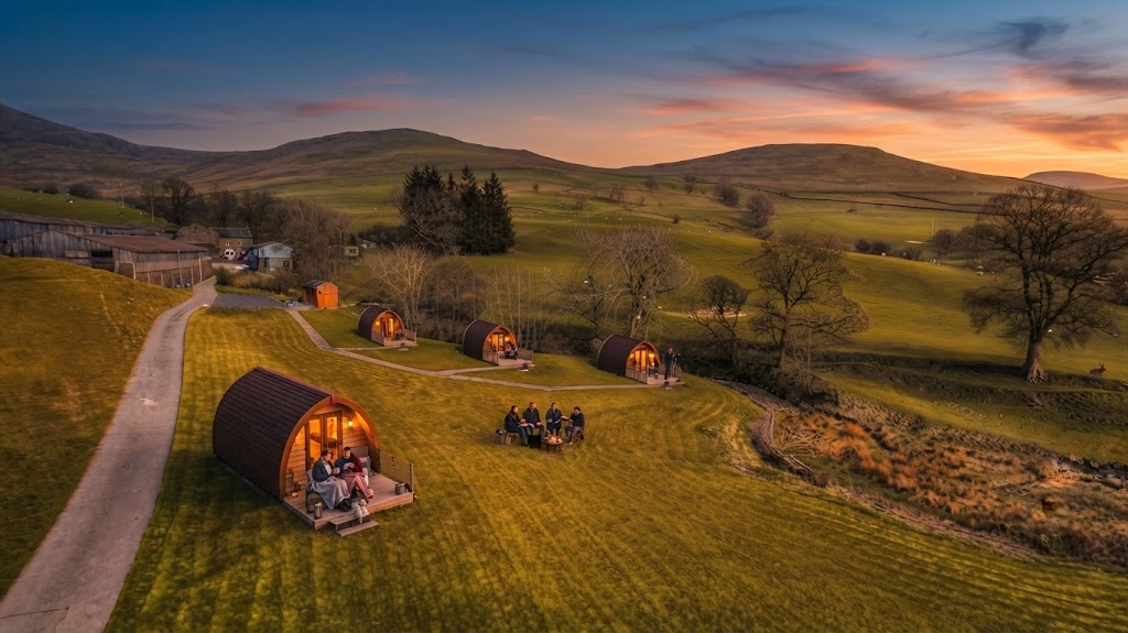 Row of curved timber camping pods on a Lake District site with fells rising behind