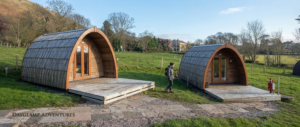 Camping cabin interior with two beds, a small table, warm lighting and a window onto a Cumbrian campsite
